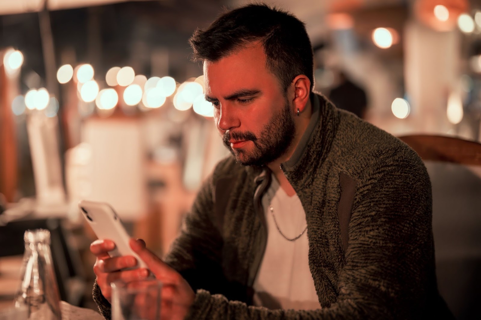 Парень сравнивает разные приложения для знакомств на телефоне с анкетами и аббревиатурами